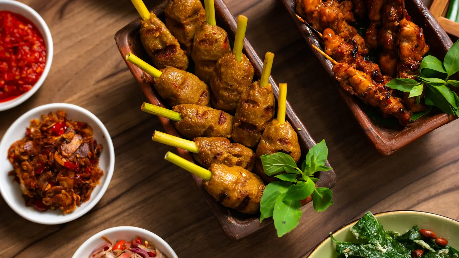 Sate, sambal, dan lauk di atas meja kayu