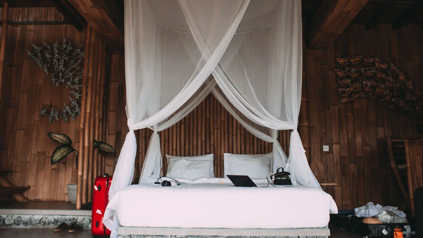Tempat tidur berseprai putih dengan dinding anyaman bambu